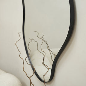 Black Metal Pond Shaped Irregular Wall Mirror on wall above branches