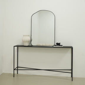 Irregular Arched Black Metal Wall Mirror beside books and vase